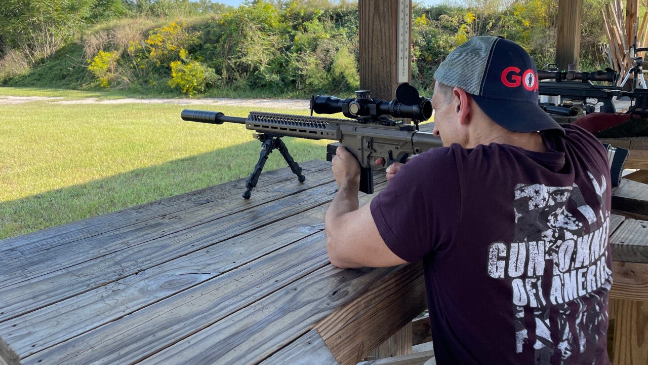 A man wearing Gun Owners of America merchandise shoots a rifle