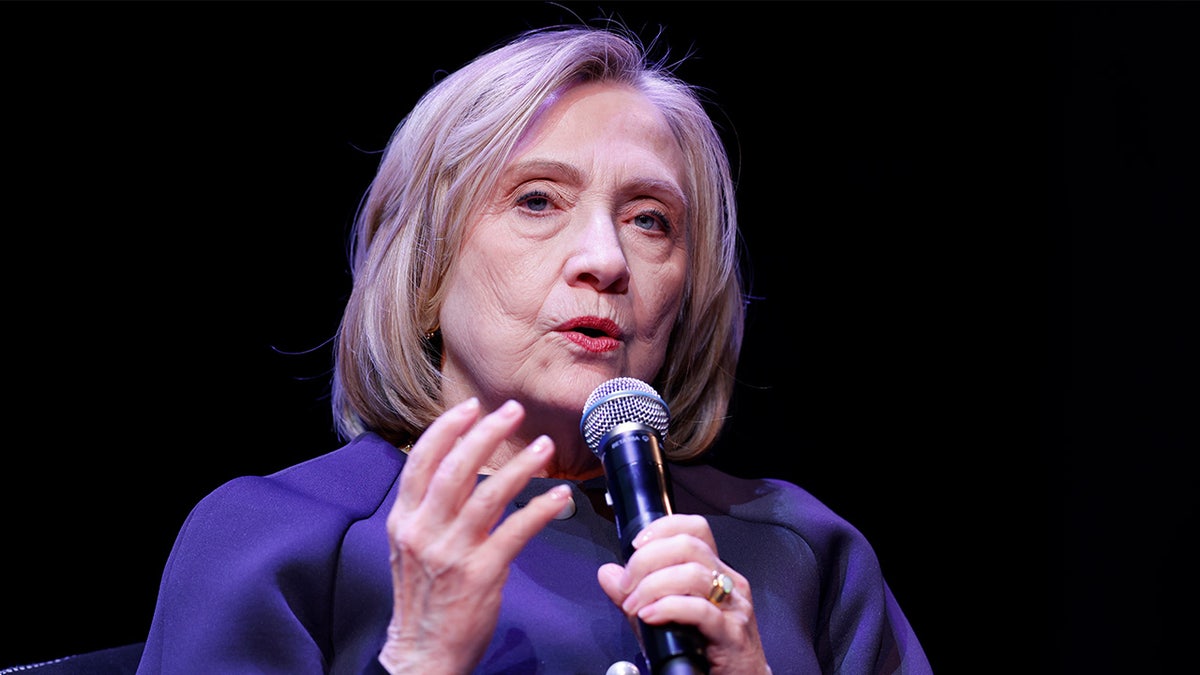 Hillary Clinton holding a microphone against a black background